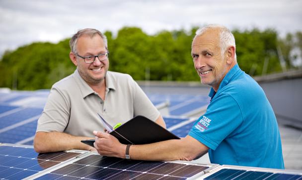 Zwei Personen stehen auf einem Dach mit Solarzellen.