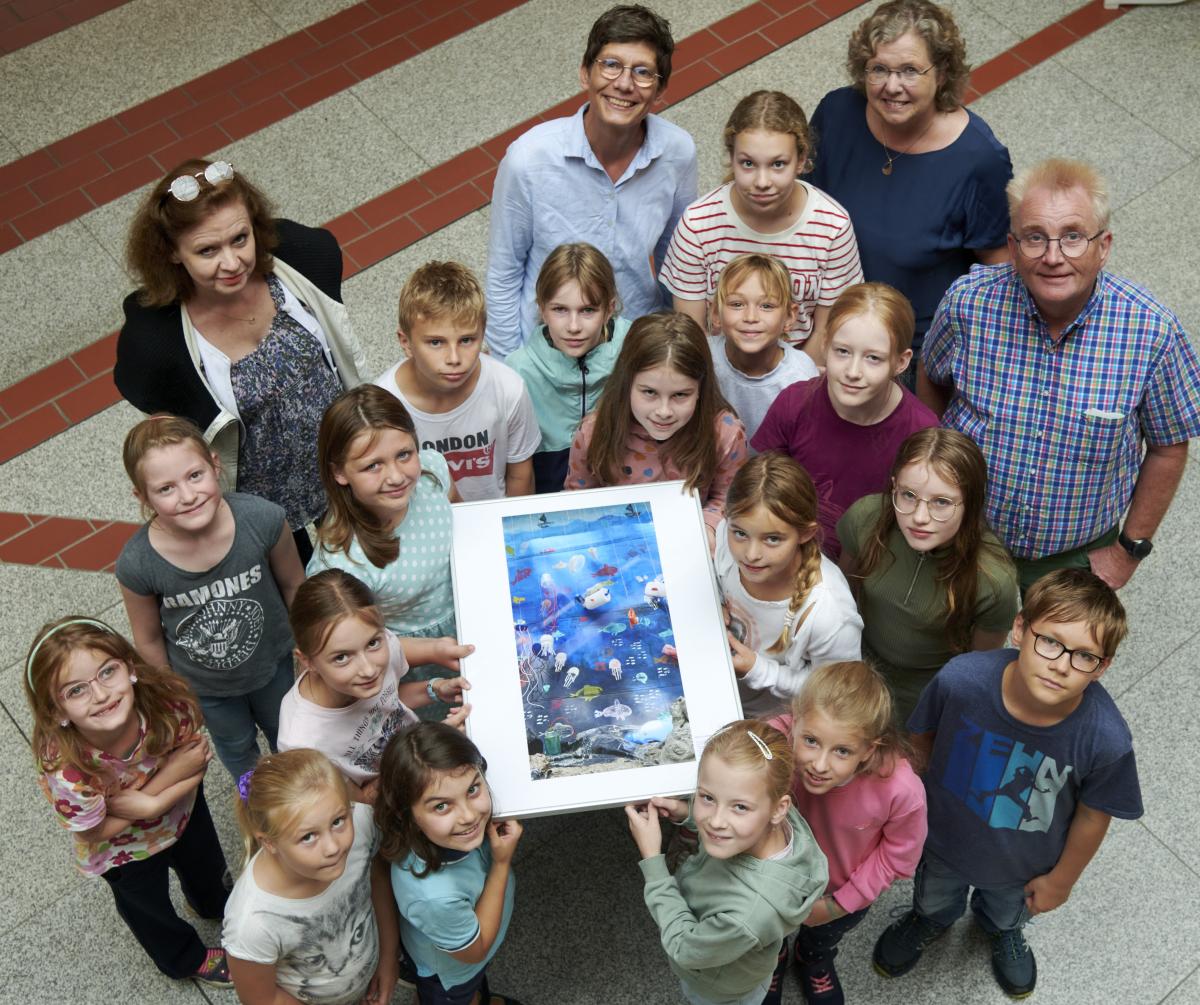 Eine Personengruppe steht in einem Foyer und schaut nach oben in die Kamera.