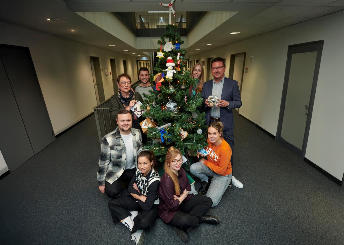 Personengruppe steht um einen Weihnachtsbaum herum.