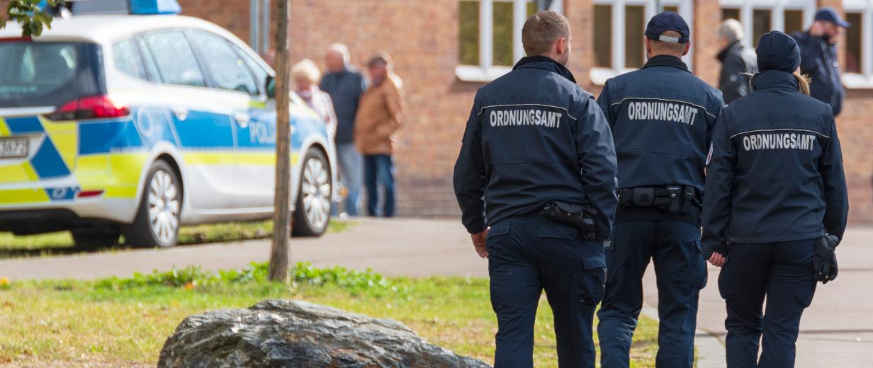 Mitarbeiter eines Ordnungsamtes auf der Straße, Polizeifahrzeug im Bild sichtbar