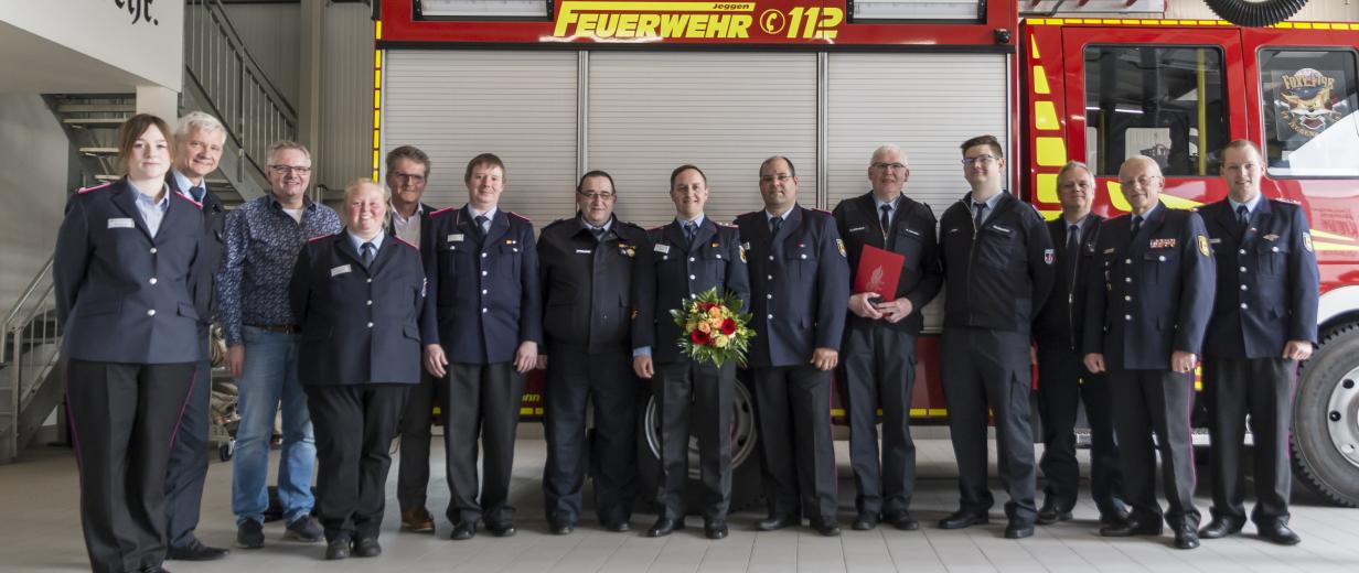 Eine Personengruppe in dunkelblauen Uniformen steht vor einem Feuerwehrfahrzeug.