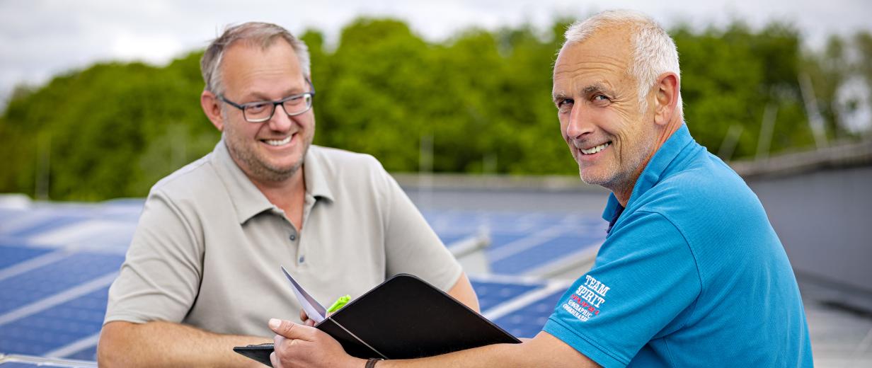 Zwei Personen stehen auf einem Dach mit Solarzellen.