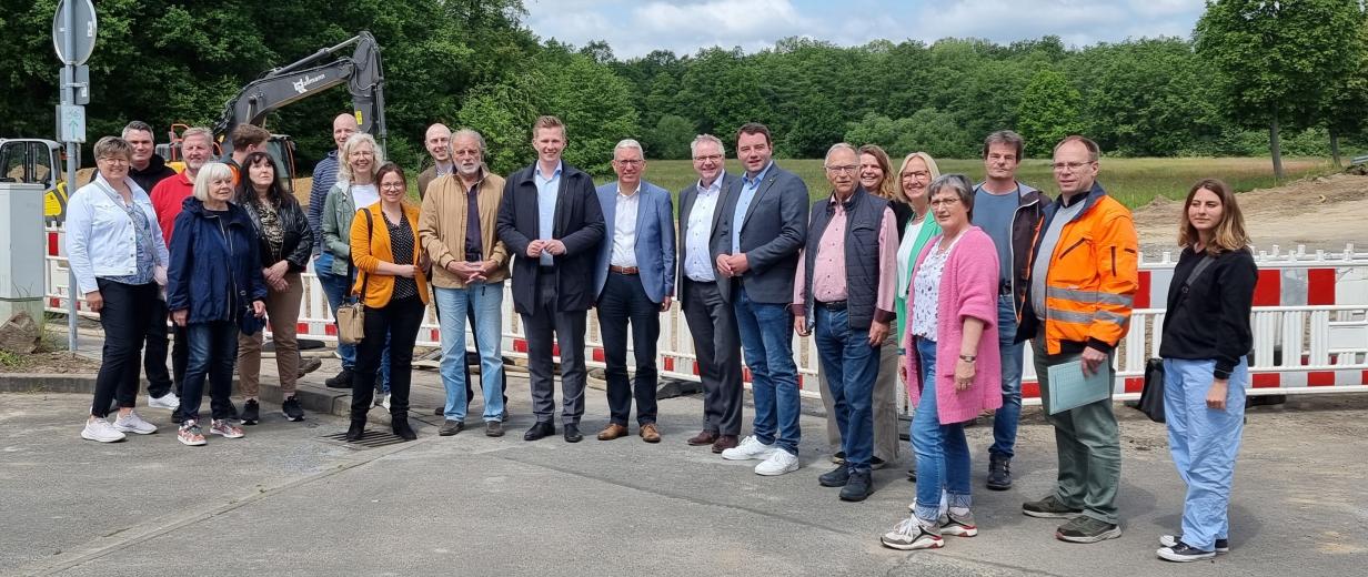 Eine Personengruppe steht vor der Absperrung einer Straßenbaustelle