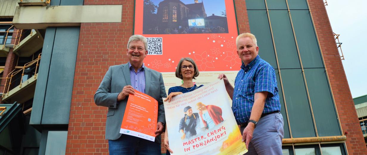 3 Personen halten ein Werbeplakat