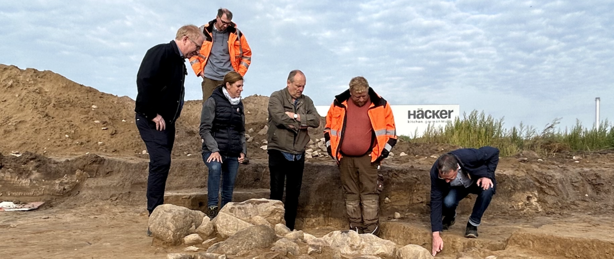 Sechs Personen stehen an einer archäologischen Grabung.