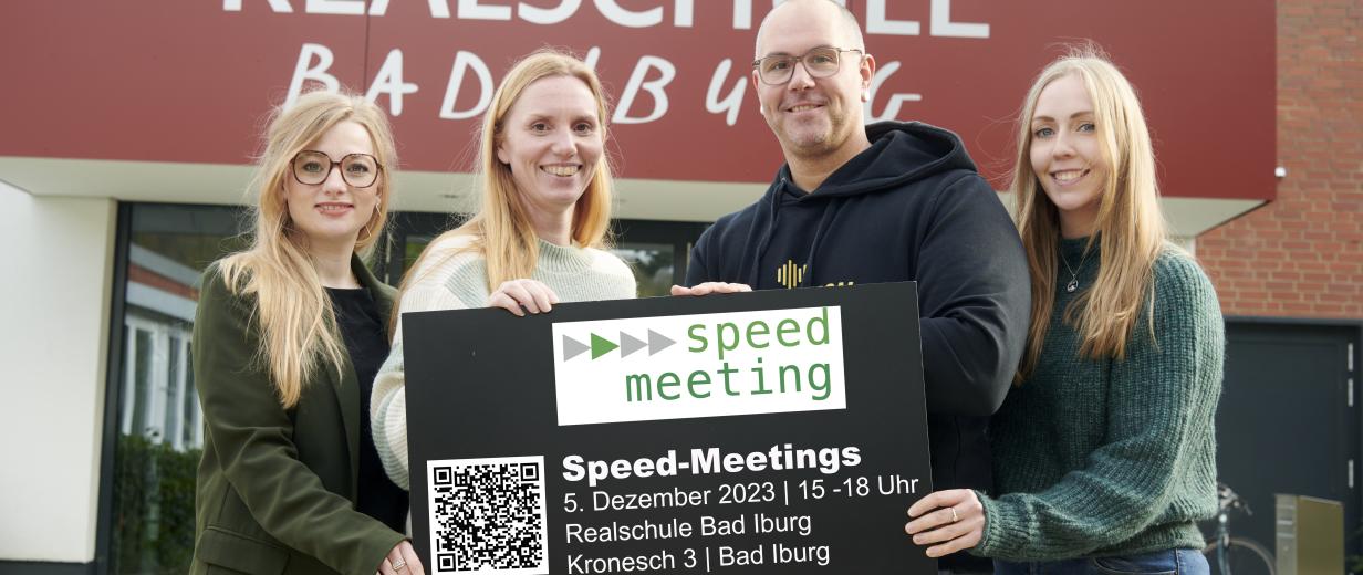 Vier Personen mit einem Schild in den Händen stehen vor einem Gebäudeeingang.