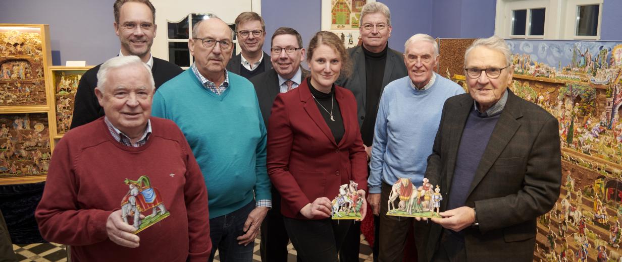 Eine Personengruppe mit Krippenfiguren in den Händen steht in einem Ausstellungsraum.