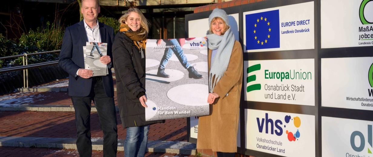 Drei Personen mit einem Plakat in den Händen stehen vor einem Gebäude.