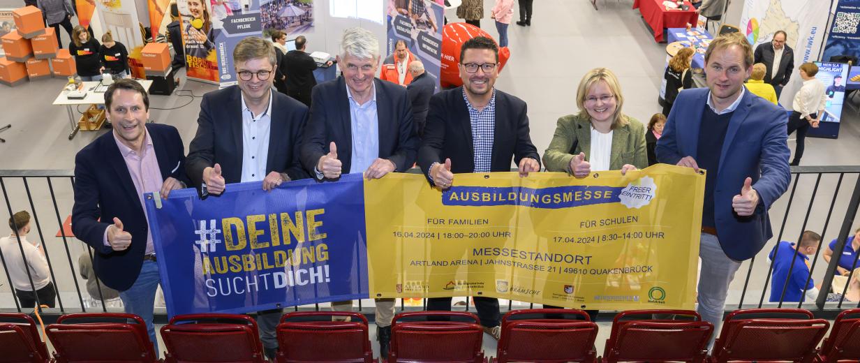 Sechs Personen mit einem Werbebanner in den Händen stehen auf der Empore einer Sporthalle.