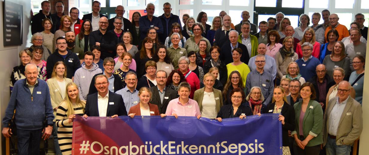 Eine große Personengruppe steht auf einer Treppe in einem Foyer.