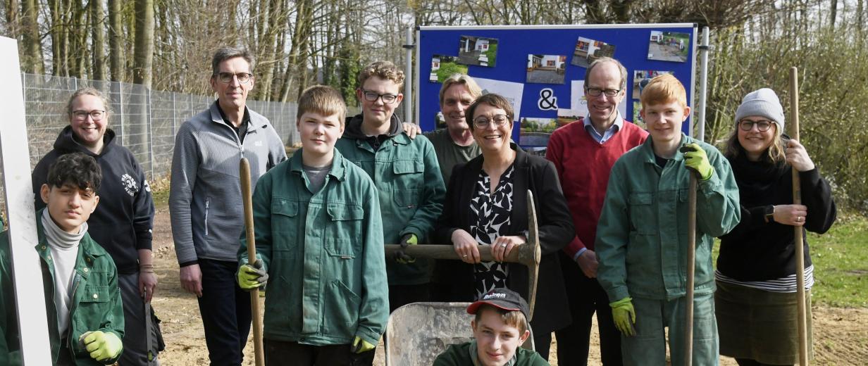 Eine Personengruppe steht mit Gartengeräten auf einer Wiese.