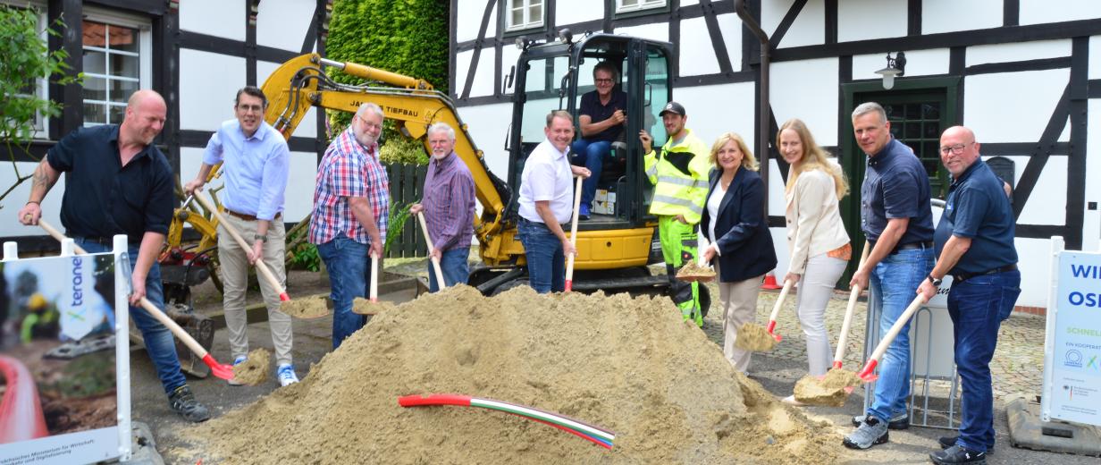 Eine Personengruppe mit Spaten in den Händen steht hinter einem Sandhaufen.