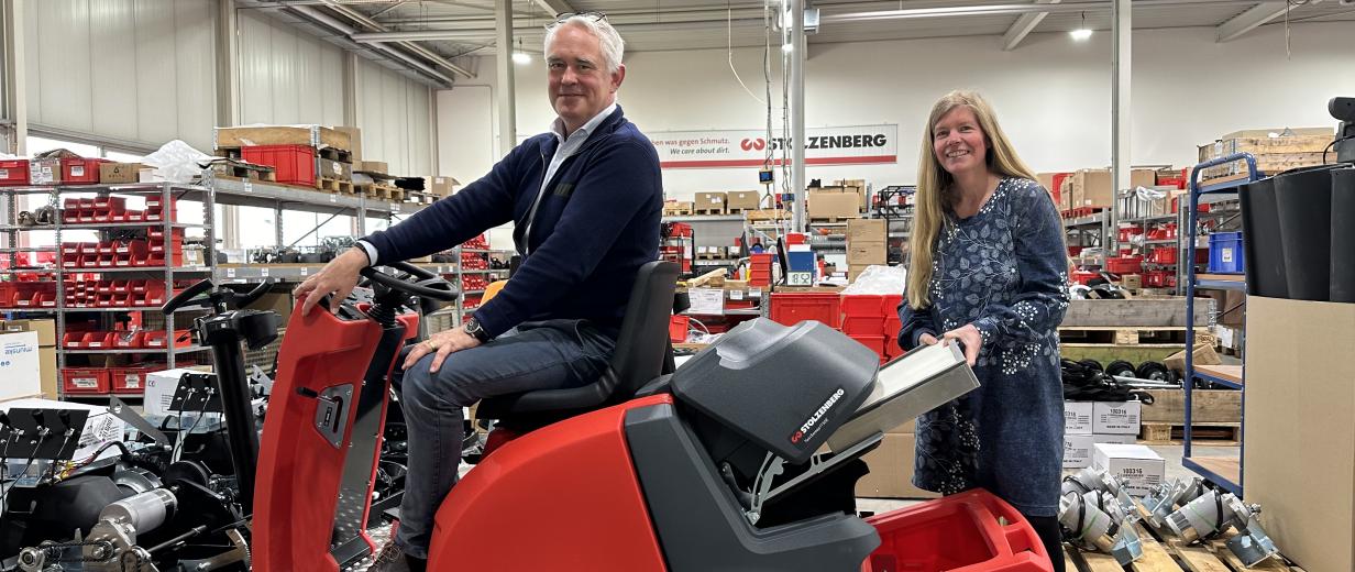 Zwei Personen mit einer Kehrmaschine in einer Werkhalle.