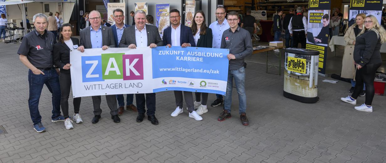 Eine Personengruppe mit Banner in den Händen steht vor einer Lagerhalle.