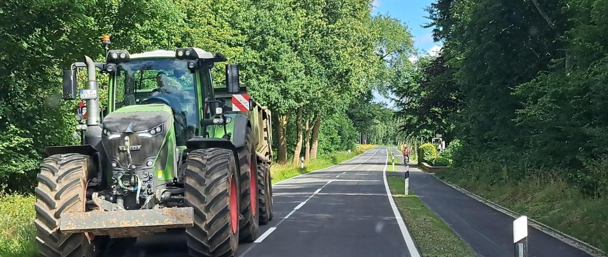 Straße mit Radweg. Auf der Straße fährt ein Traktor.