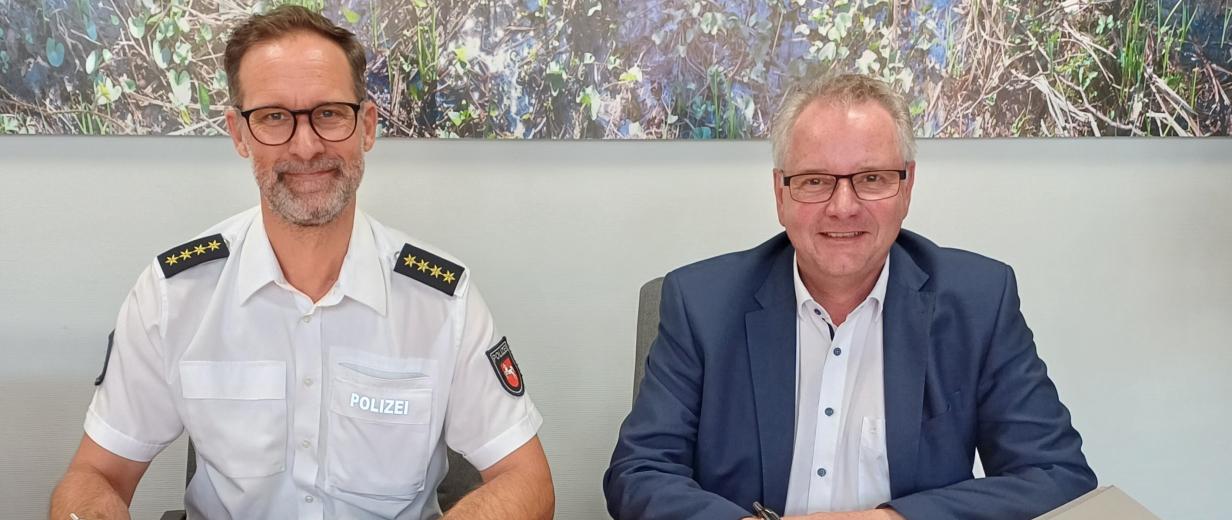 Zwei Personen mit Stift in der Hand sitzen an einem Tisch vor sich Unterschriftenmappen.