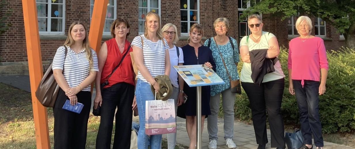 Eine Personengruppe steht vor einem Backsteingebäude.