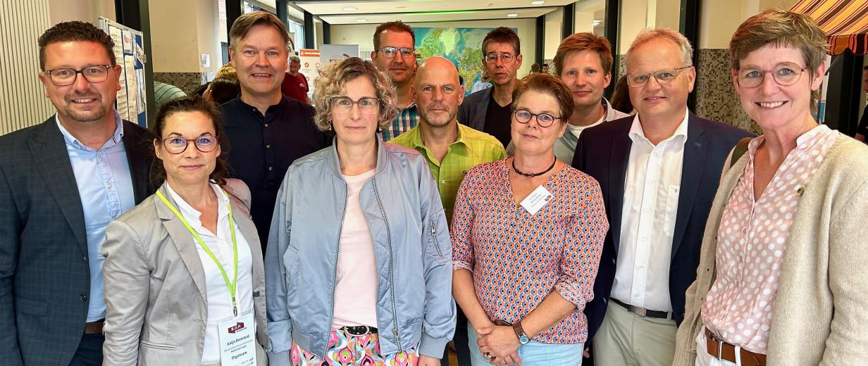 Eine Personengruppe schaut im Halbkreis stehend in die Kamera.