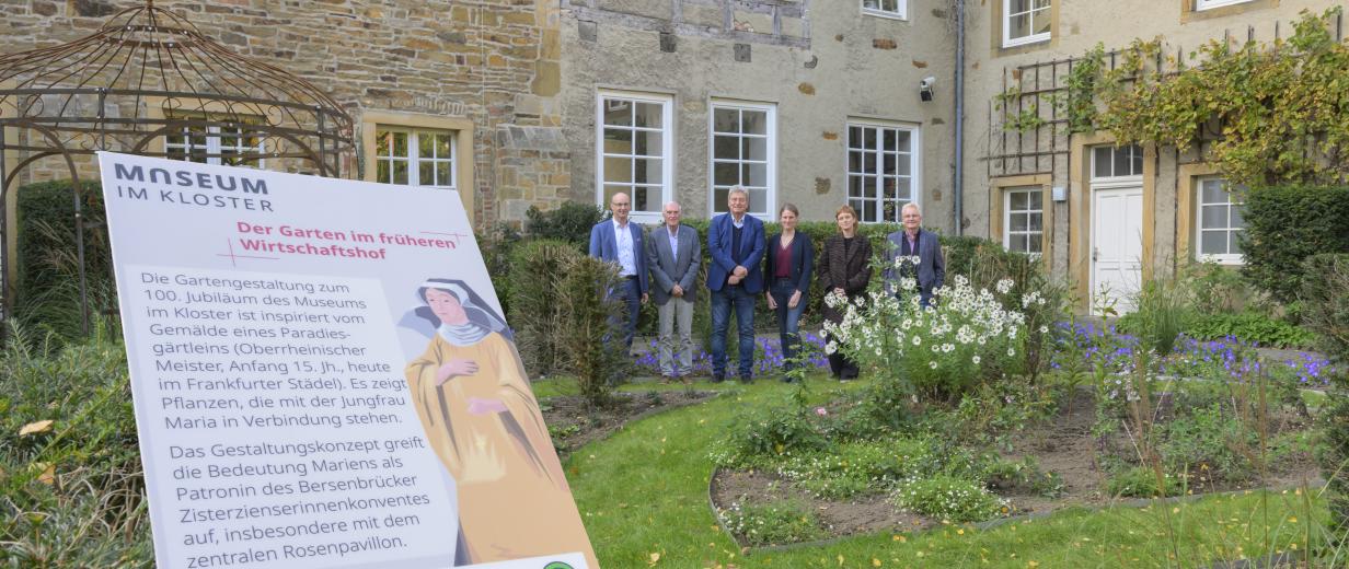 Eine Personengruppe steht in einem Gartenvor einem historischen Gebäude.