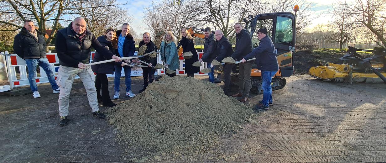 Eine Personengruppe mit Spaten in der Hand steht hinter einem Sandhaufen.