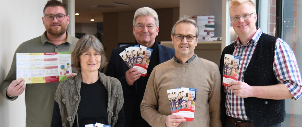 Fünf Personen stehen in einem Flur und halten Flyer in den Händen.