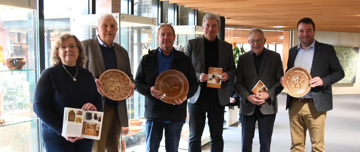 Sechs Personen mit Keramiktellern in den Händen stehen in einem Foyer vor Vitrinen.