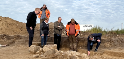 Sechs Personen stehen an einer archäologischen Grabung.