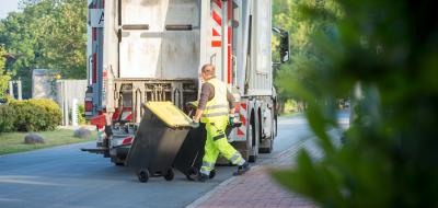 Eine Person rollt eine gelbe Tonne zu einem Abfallfahrzeug.