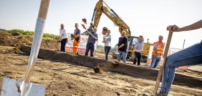 Eine Personengruppe mit Spaten in den Händen steht auf einer Baustelle.