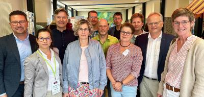 Eine Personengruppe schaut im Halbkreis stehend in die Kamera.