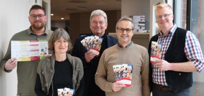 Fünf Personen stehen in einem Flur und halten Flyer in den Händen.