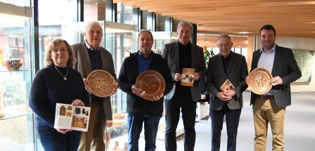 Sechs Personen mit Keramiktellern in den Händen stehen in einem Foyer vor Vitrinen.