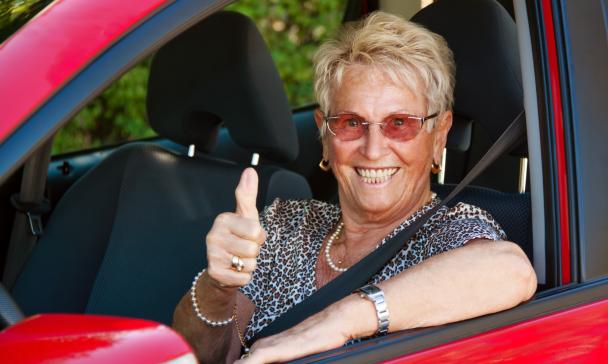 Eine Seniorin sitz in einem Auto, schaut zur Seite und hebt den rechten Daumen.