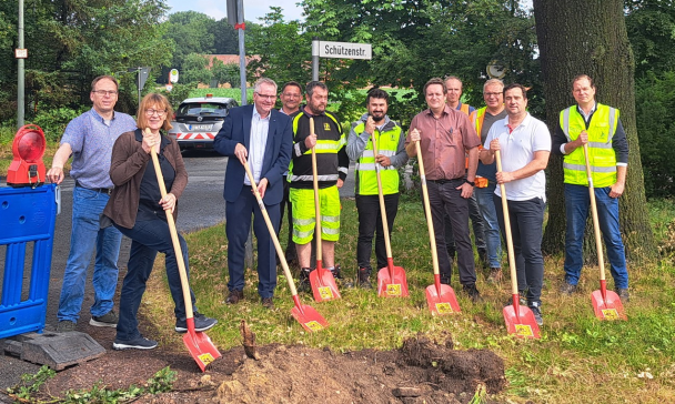 Eine Personengruppe mit schaufeln in den Händen steht an einer Straßenbaustelle.