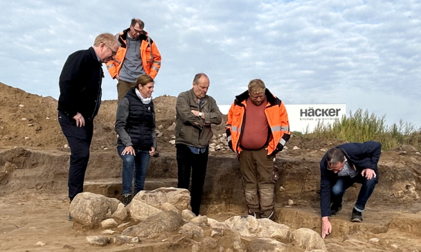 Sechs Personen stehen an einer archäologischen Grabung.