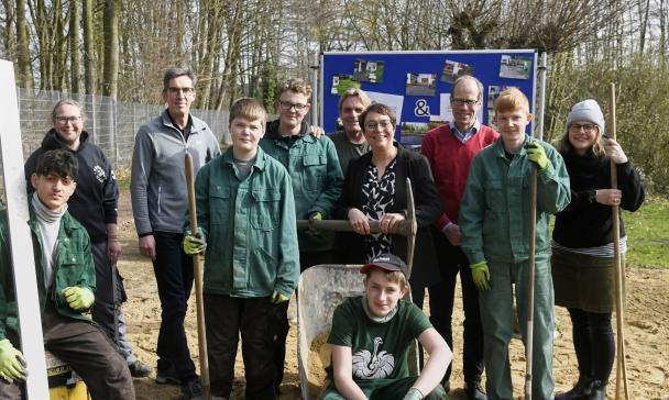 Eine Personengruppe steht mit Gartengeräten auf einer Wiese.